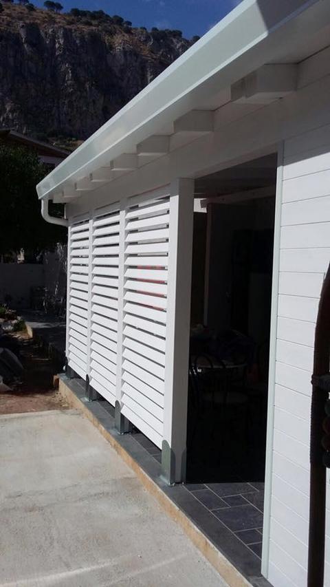 Veranda addossata in legno lamellare impregnato Bianco una mano con pareti chiuse da frangisole.