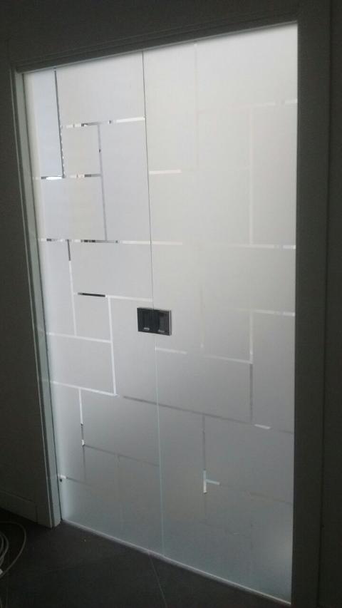 Porta in vetro temperato 8mm trasparente decori rettangolari, disposti in varie angolazioni, lavorati in sabbiatura, lasciando uno spazio fra le figure geomentriche di 1cm in trasparenza. In seguito è stato applicato su tutta la superficie un prodotto acidante per rendere satinata la parte in sabbiatura. Maniglie e accessori in acciaio.