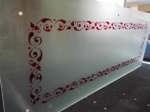 Vetro satinato 5mm con greca che funge da cornice interna scavata e colorata nei toni del rosso e nelle sue sfumature.