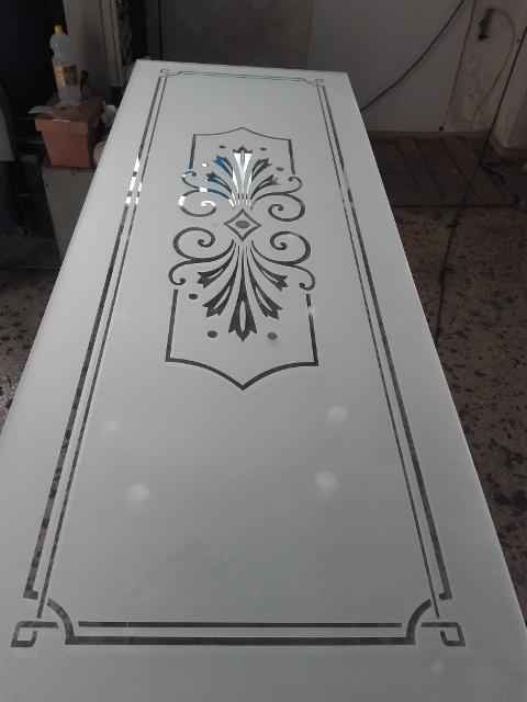 Vetro 4mm trasparente lavorato in sabbiatura, arricchito da una doppia cornice di diverso spessore che segue il perimetro del vetro e un motivo decorativo posto internamente ad essa. Entrambi gli elementi sono sati lasciati in trasparenza.