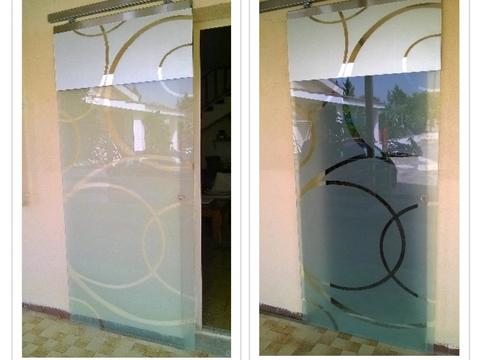 Porta scorrevole con vetro sabbiato decorato con motivi circolari lucidi, su binario in acciaio.