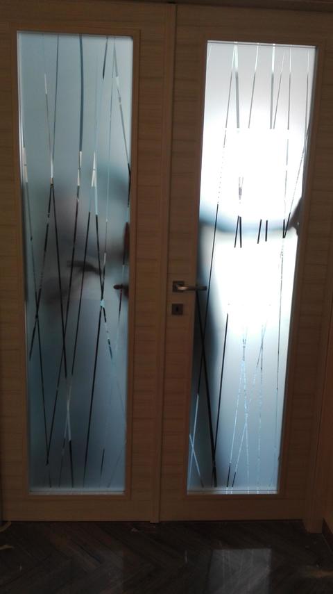 Vetri incorniciati dal telaio della porta con decoro a strisce trasparenti in contrasto dal satinato dello sfondo.